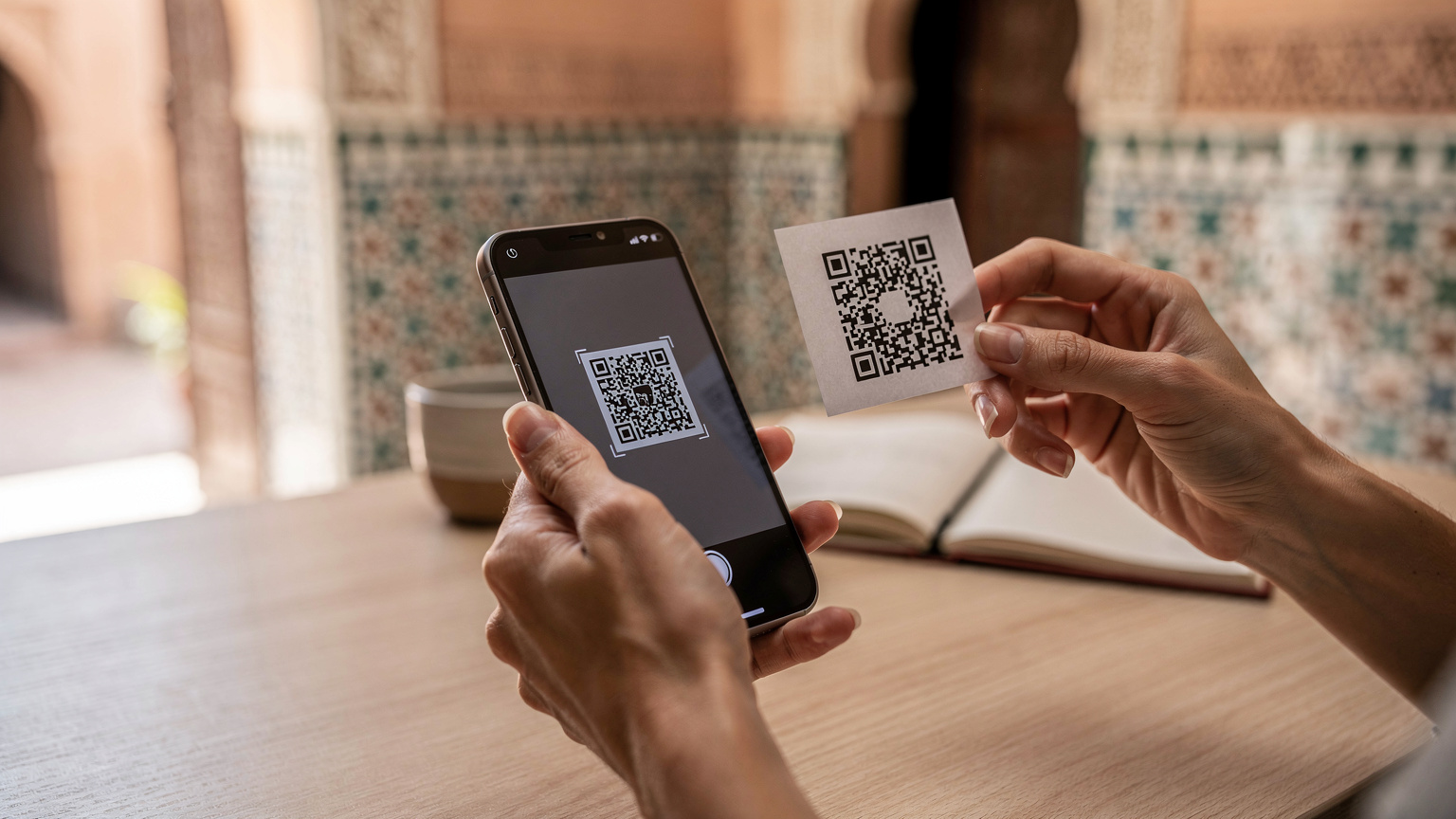 A woman's hands holding a smartphone, with a QR code on a separate screen or paper being scanned by the phone's camera, showing the eSIM activation process.