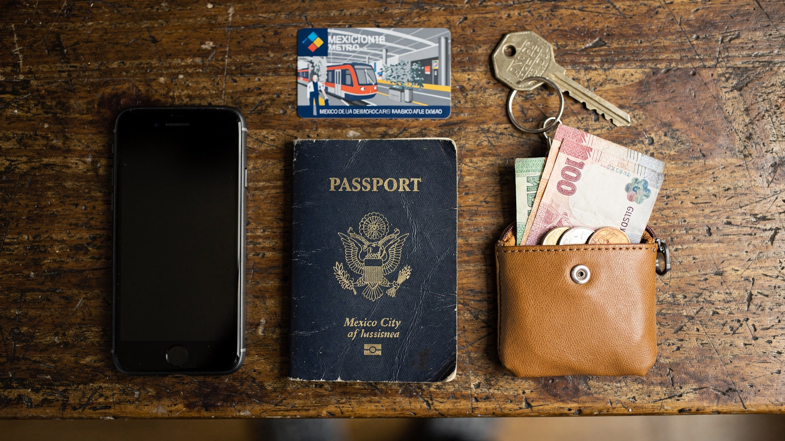 A close-up, overhead flat-lay shot of travel essentials: a passport, a smartphone, a small pouch of pesos, and a metro card, all resting on a rustic wooden table, ready for a day of exploration.