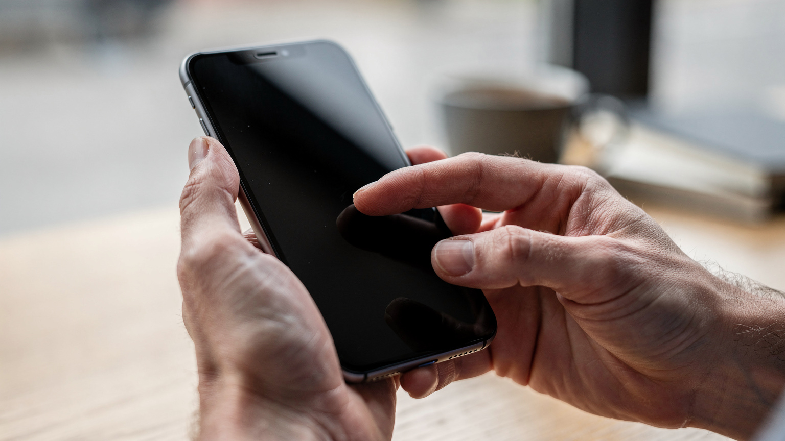 Close-up of hands holding a smartphone, with one finger gently tapping the screen, showing the interaction without revealing specific UI or text.