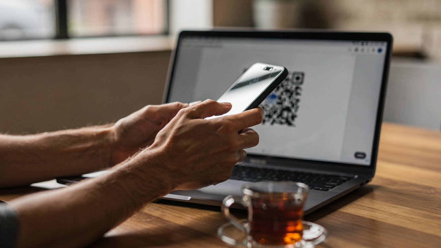 Bir kafenin penceresinden içeri süzülen doğal ışık altında, bir kişinin elleri bir akıllı telefonu tutarken eSIM QR kodunu tarama anını gösteriyor, ekranda belirsiz bir kurulum arayüzü var.