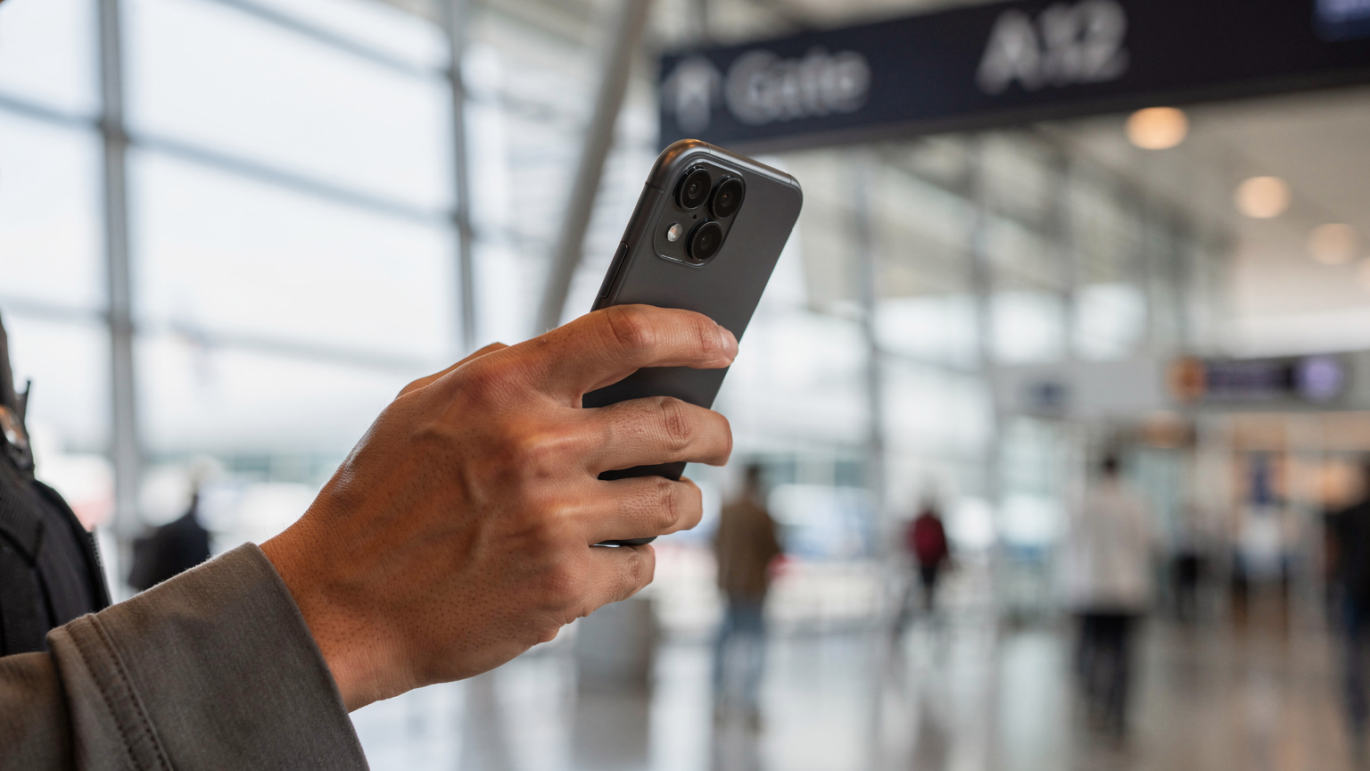 Bir gezginin eli, bir akıllı telefonun ekranında eSIM QR kodunu tararken gösteriliyor, arka planda bulanık bir havaalanı terminali beliriyor.