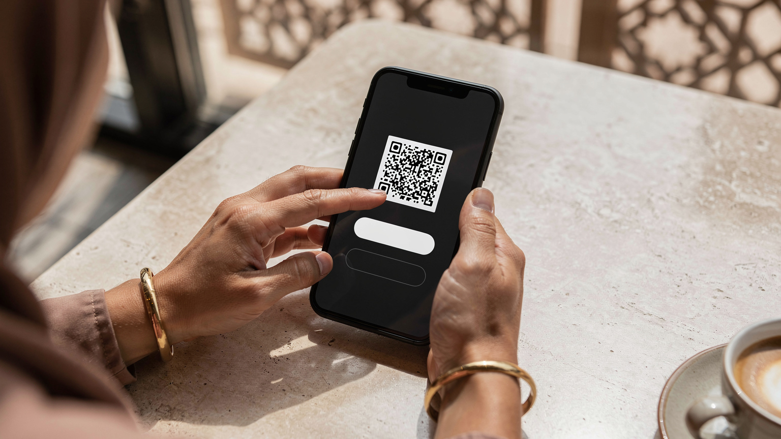يد امرأة تحمل هاتفًا ذكيًا يعرض رمز QR لتفعيل eSIM في مقهى حديث في حي الدرعية التاريخي بالرياض.